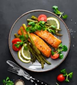 Laks med grillede asparges, cherrytomater og citron på tallerken.