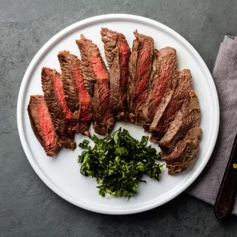 Saftig, skåret grillet oksekød med friske krydderurter på en hvid tallerken.