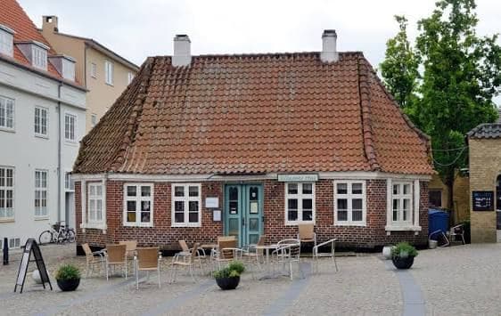 Sillasens Hus på Varde Torv med rødt valmet tag, to hvide skorstene, skrå hjørner og blå dør