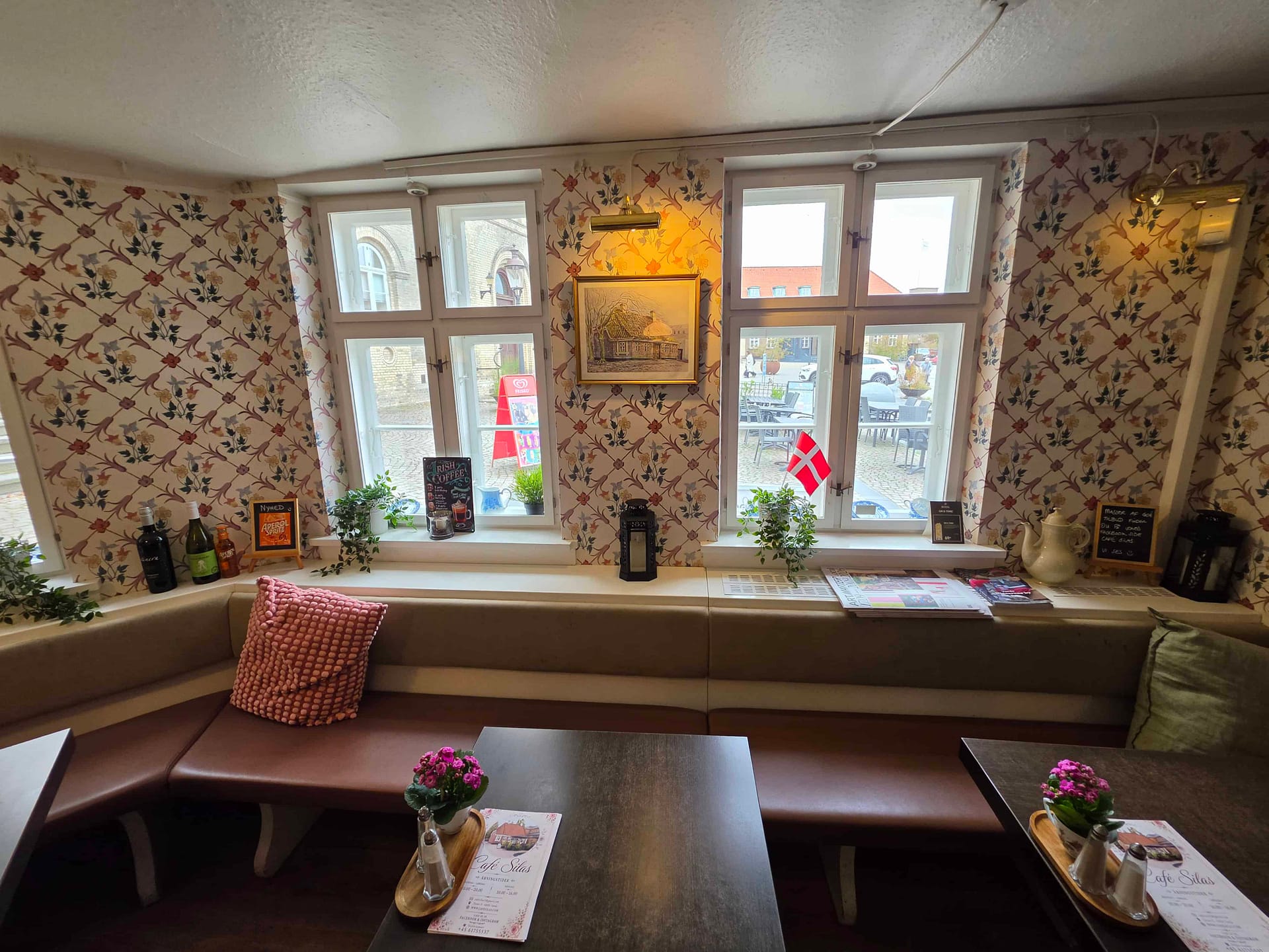Spisestuen i Café Silas med mørke borde, sorte lænestole, blomstertapet, gamle fotografier på væggen og hængende olielamper